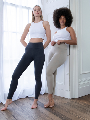 Two Model wearing the Everyday High Waisted Legging In colours Infinity Blue Marl and Oatmeal Beige. They are standing indoors, next to a white window and one model is leaning against a white wall.